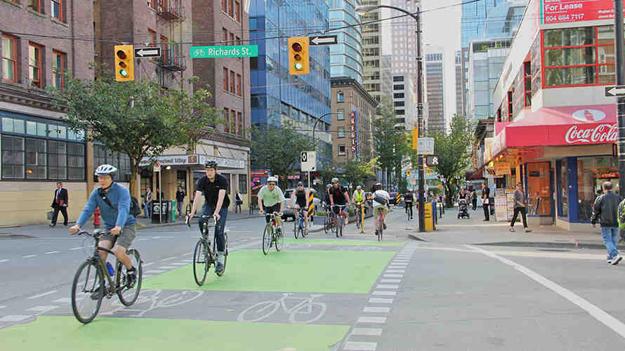 A group of commuters bike through a crosswalk in a city. Photo: Paul Kreuger.