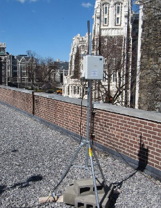 Picture of an air monitor box mounted on a pole on a roof. 