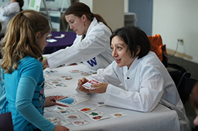 A DEOHS student talks with a child across a table at the Paws-on Science event in the Pacific Science Center.