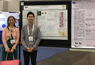 A woman and man stand smiling in front of a research poster.