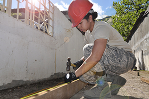 Female construction worker hammering a nail into a wooden board outdoors Female construction worker hammering a nail into a wooden board outdoors