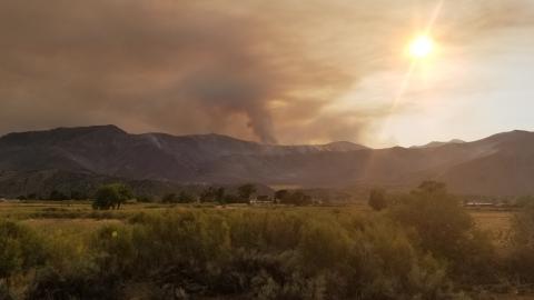 Wildfire smoke behind a mountainous landscape with fields in the foreground.