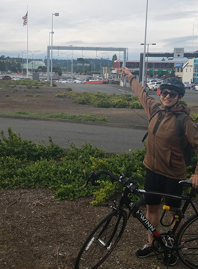 Man standing next to his bicycle points to a border crossing behind him.