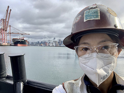 Photo of Amy Liu wearing a face mask with a port and waterfront behind her.