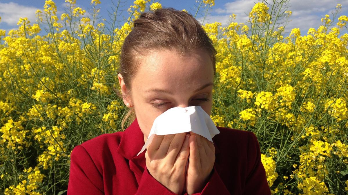 Woman sneezing into tissue in front of field of flowers