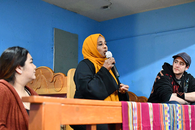 A panelist in an orange hijab talks into a microphone.