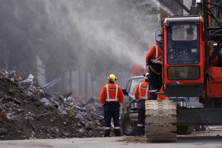 Emergency response personnel stand by a truck spraying water on rubble