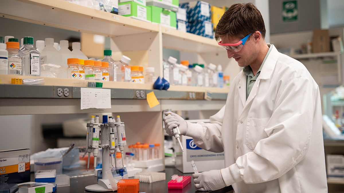 Student in a white lab coat working in a lab. 