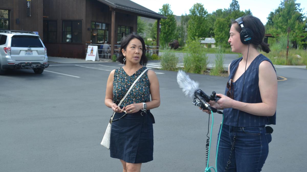 A freelance journalist holds a large microphone up to a woman who is talking