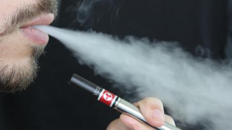 A man holds an e-cigarette while exhaling smoke.