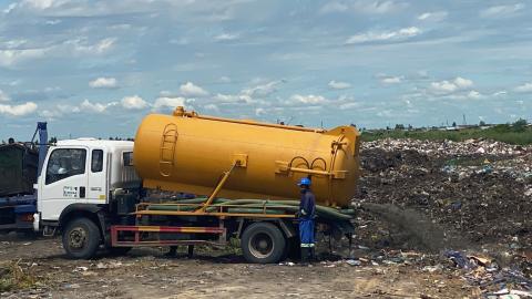 A truck with a large yellow tank empties fecal sludge at a waste site. 