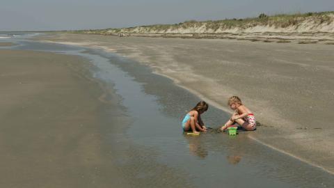 Two young children play in the sand on a beach