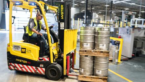 Person Driving Yellow Forklift Carrying Metal Barrels