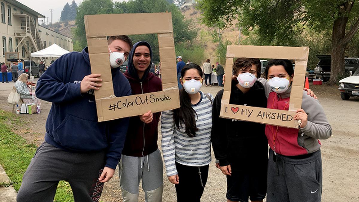 Five people (four in N95 masks) pose with cardboard picture frame cutouts saying "#ColorOutSmoke" and "I [heart] MY AIRSHED."