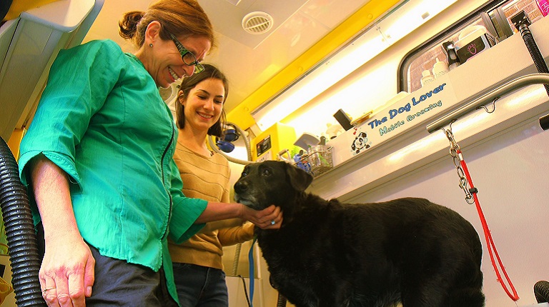 Two women petting a black dog in a mobile greeting van