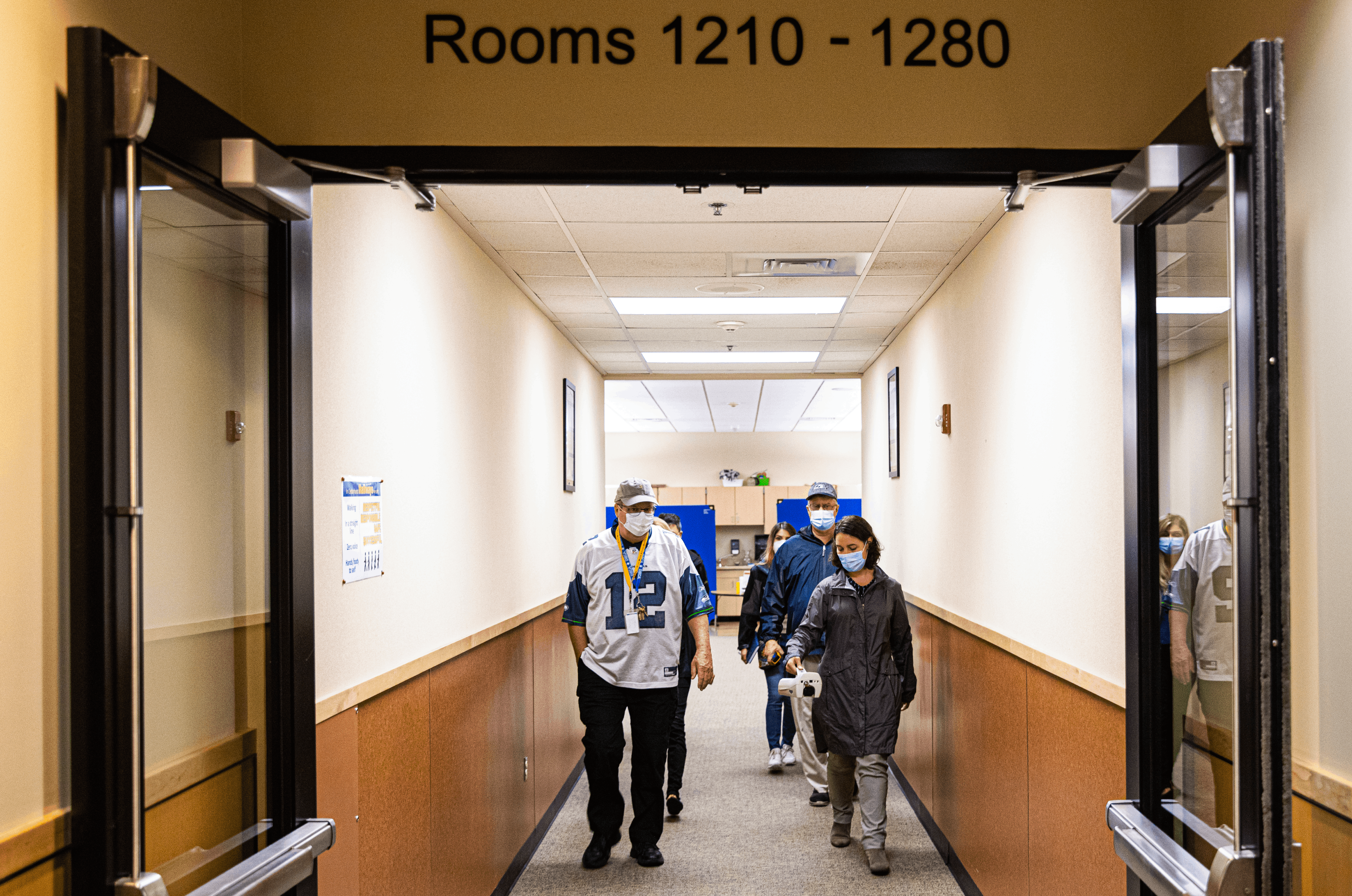 A group of people walk down a school hallway.
