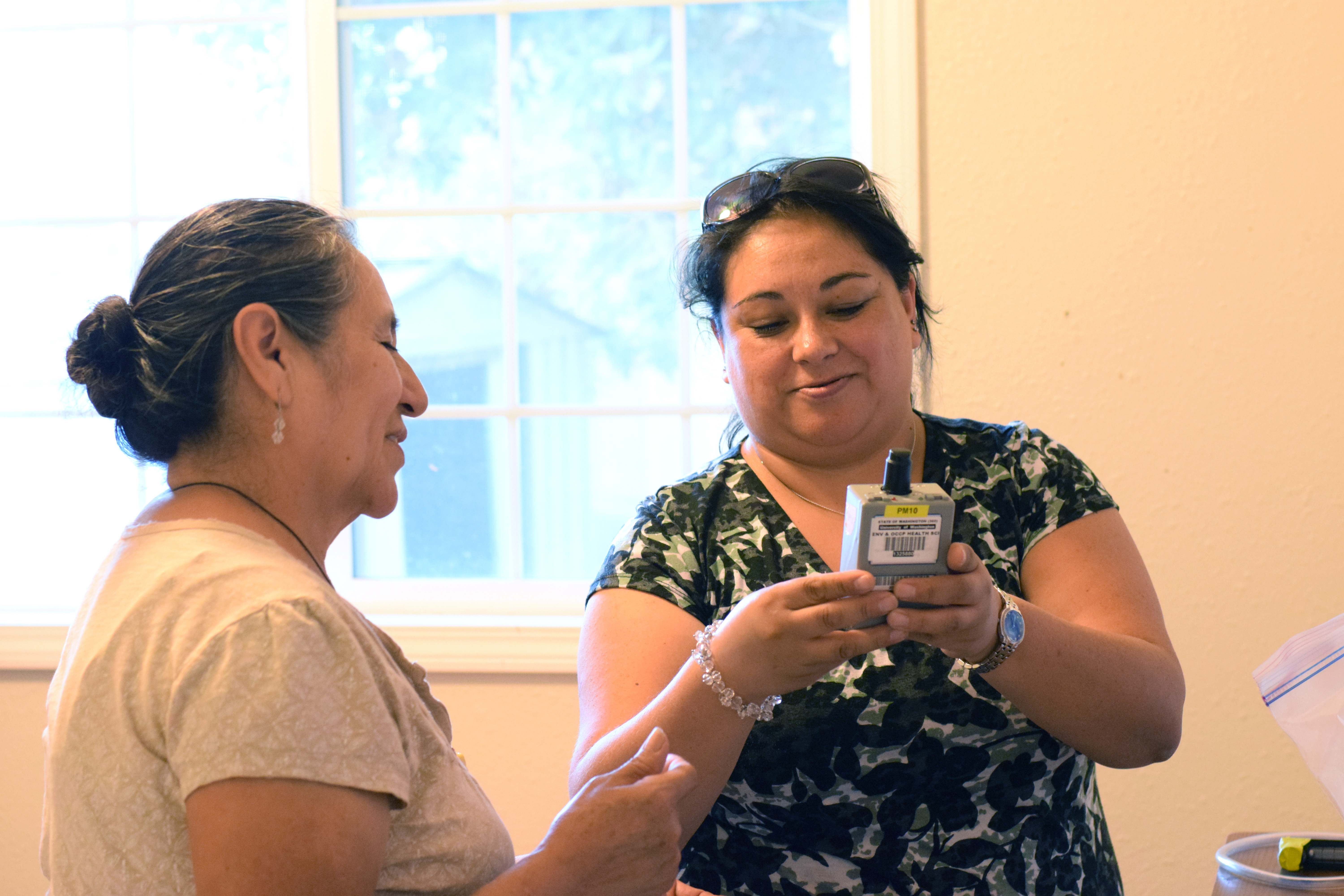 Elizabeth Torres (right) and Carmen Mireles of Northwest Communities Education Center/Radio KDNA prepare to install sensors to measure particulate matter in a study home.