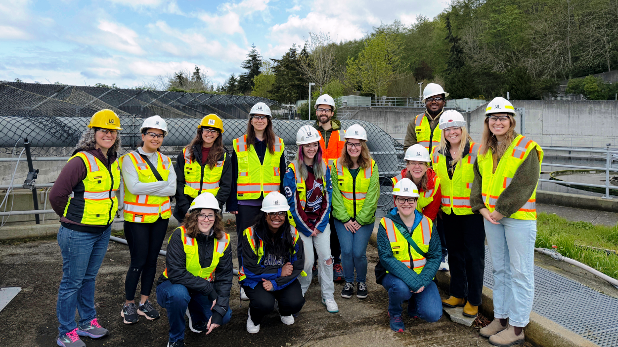 A large group of people in hard hats and safety vests stand in front of a wastewater treatment facility in Seattle.