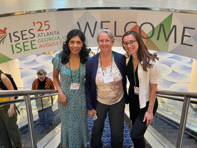 Magali Blanco, Lianne Sheppard and Rachel Shaffer stand together in front of a sign reading ISEE '25, Atlanta, Georgia, Welcome.
