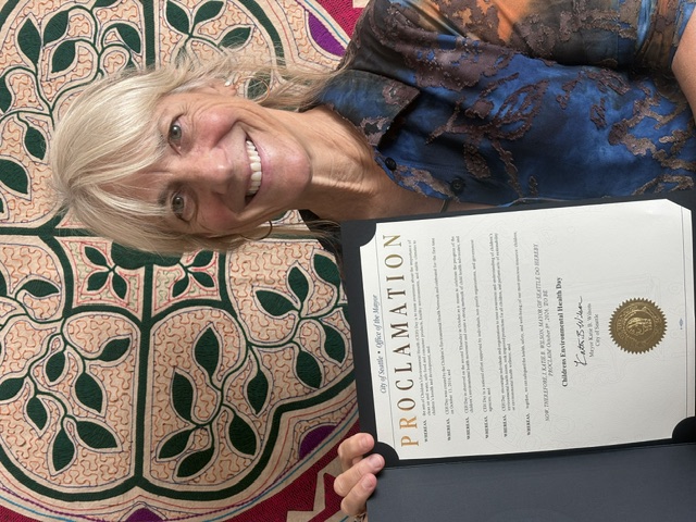 Catherine Karr holds a copy of a proclamation from Seattle Mayor Katie Wilson declaring October 8 Children's Environmental Health Day.