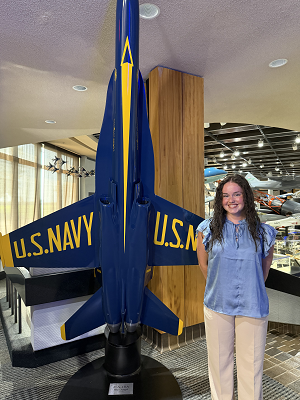 Lauren Costa stands in front of a U.S. Navy aircraft displayed vertically.