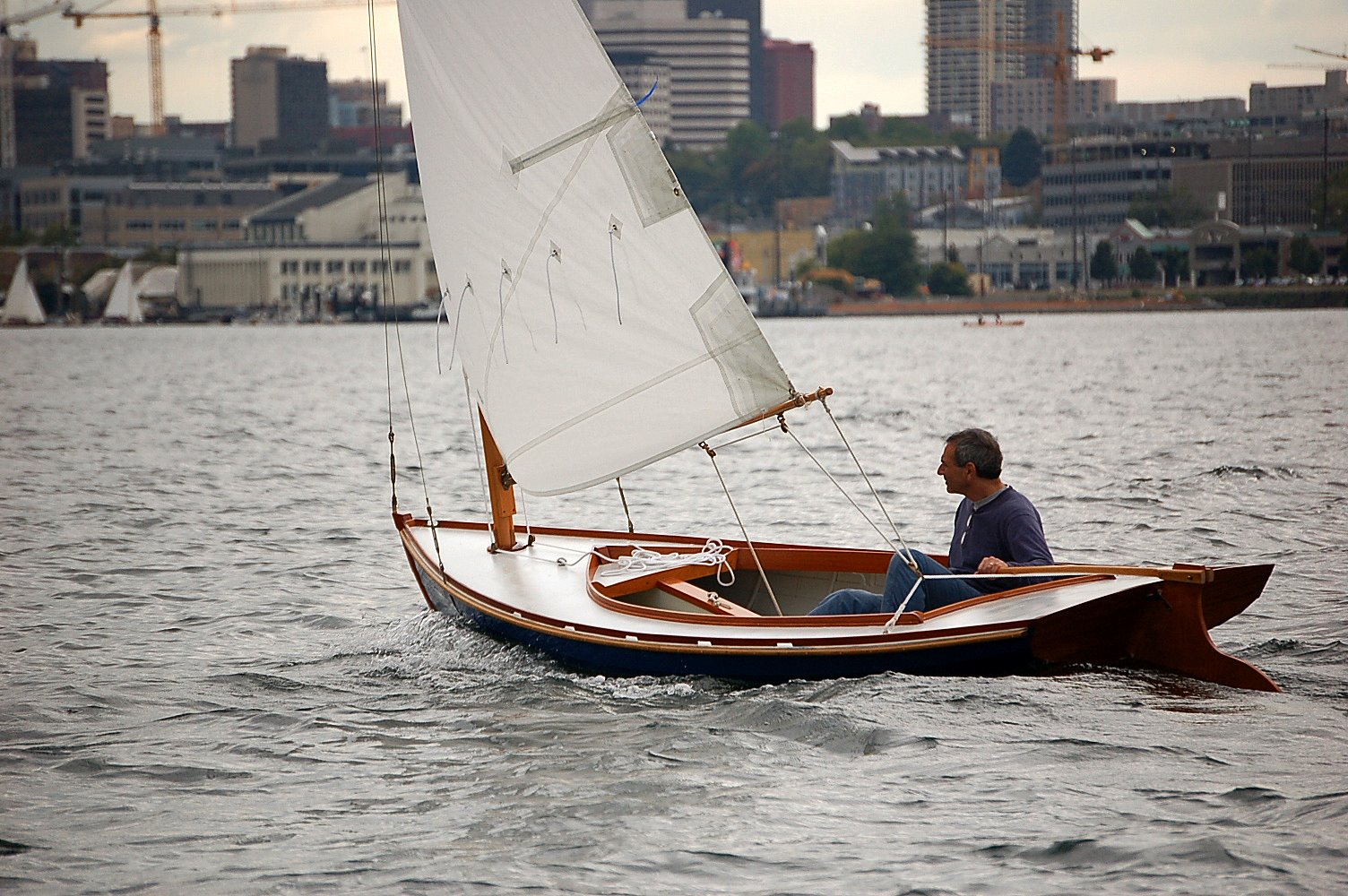 A man sails a sailboat on a lake.