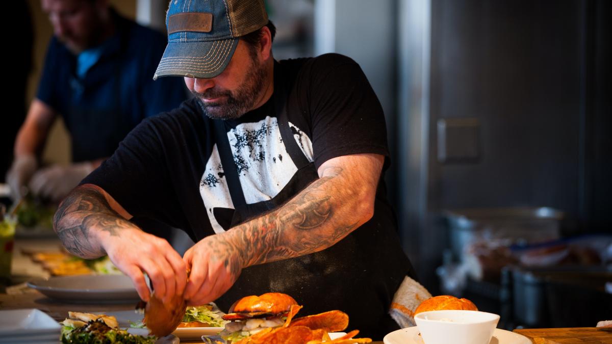 Person with arm tattoos preparing burgers behind the counter at a restaurant.