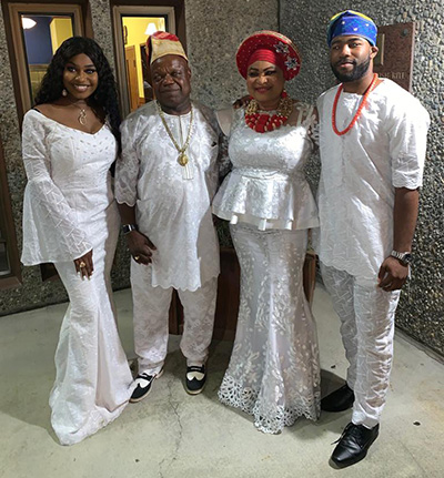 Four people wearing white clothes pose next to each other against a stone wall.