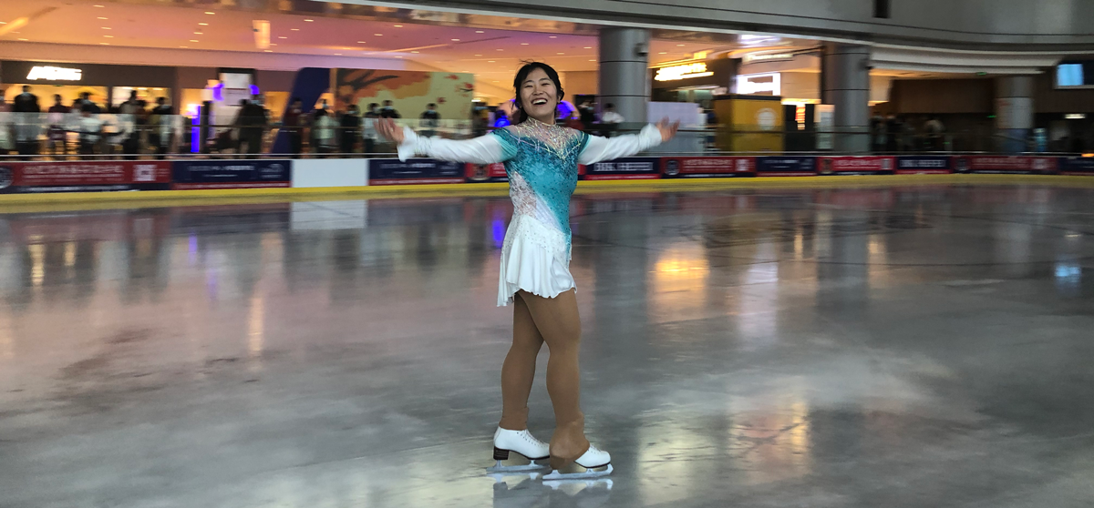 Woman figure skating in a rink with her arms outstretched.