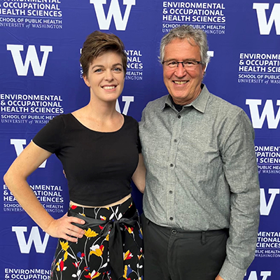 Burbacher stands next to advisee Alicia Hendrix in front of a UW background.