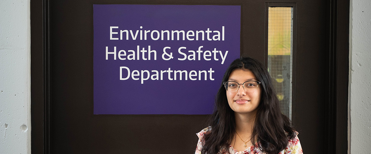 Anika Rajput stands in front of a sign reading "Environmental Health & Safety Department"