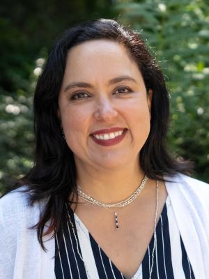 Diana Ceballos smiles outside in front of greenery.