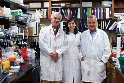 Three people in white lab coats stand in a laboratory.