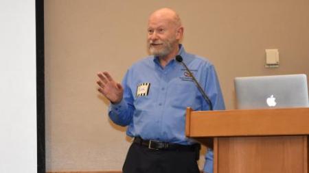 A man in a blue shirt gestures near a podium.