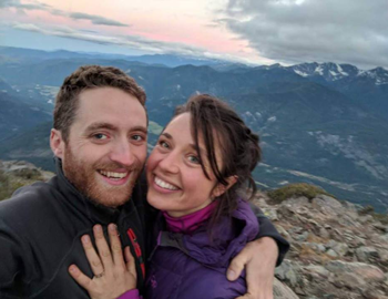 Close-up of a man and woman embracing on top of a mountain at sunset.