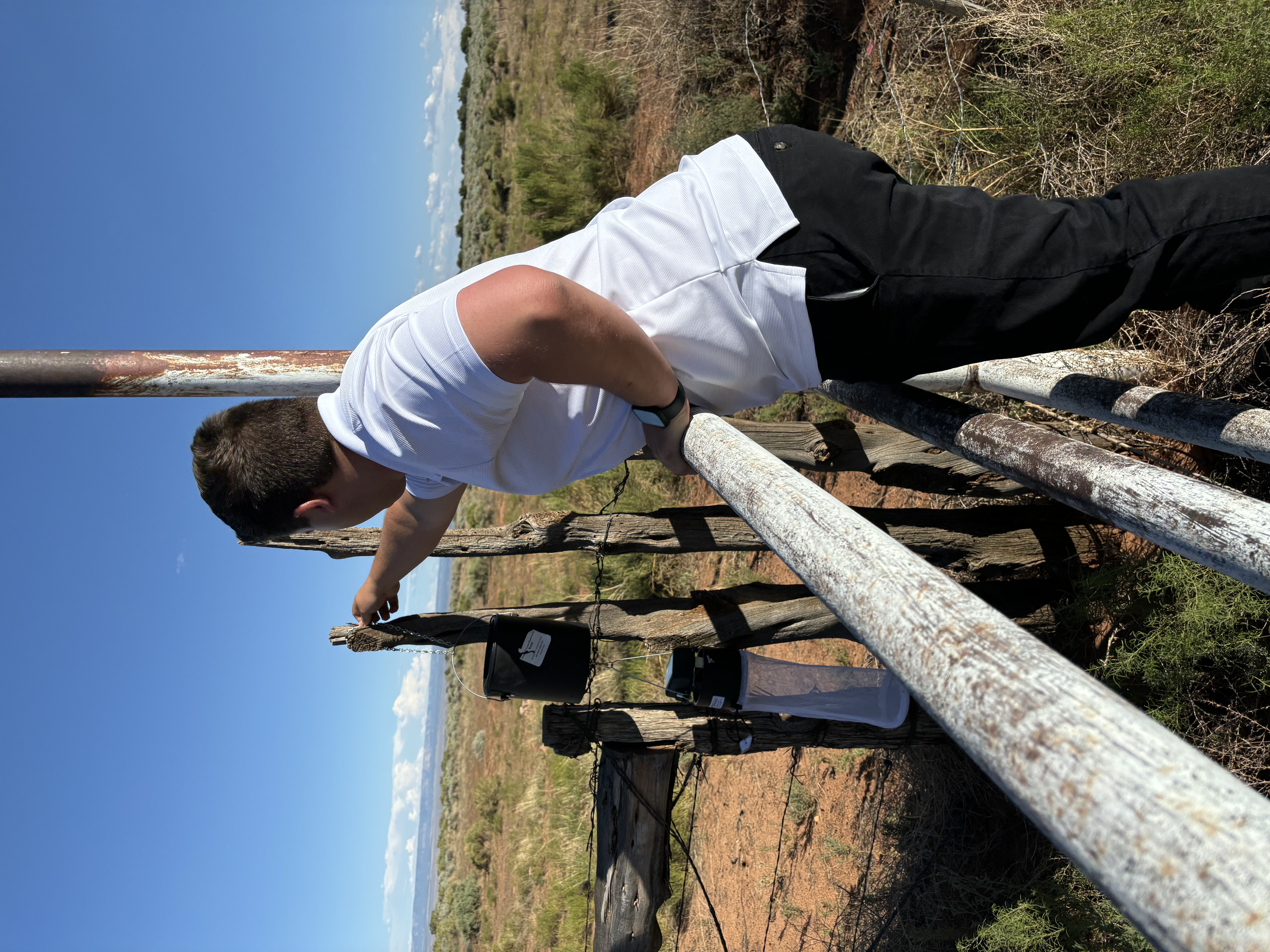 Jorge checks equipment in the field by leaning over a fence post