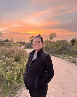 Photo of Shelley Stephan standing outside and smiling at sunset on a path with plantings.