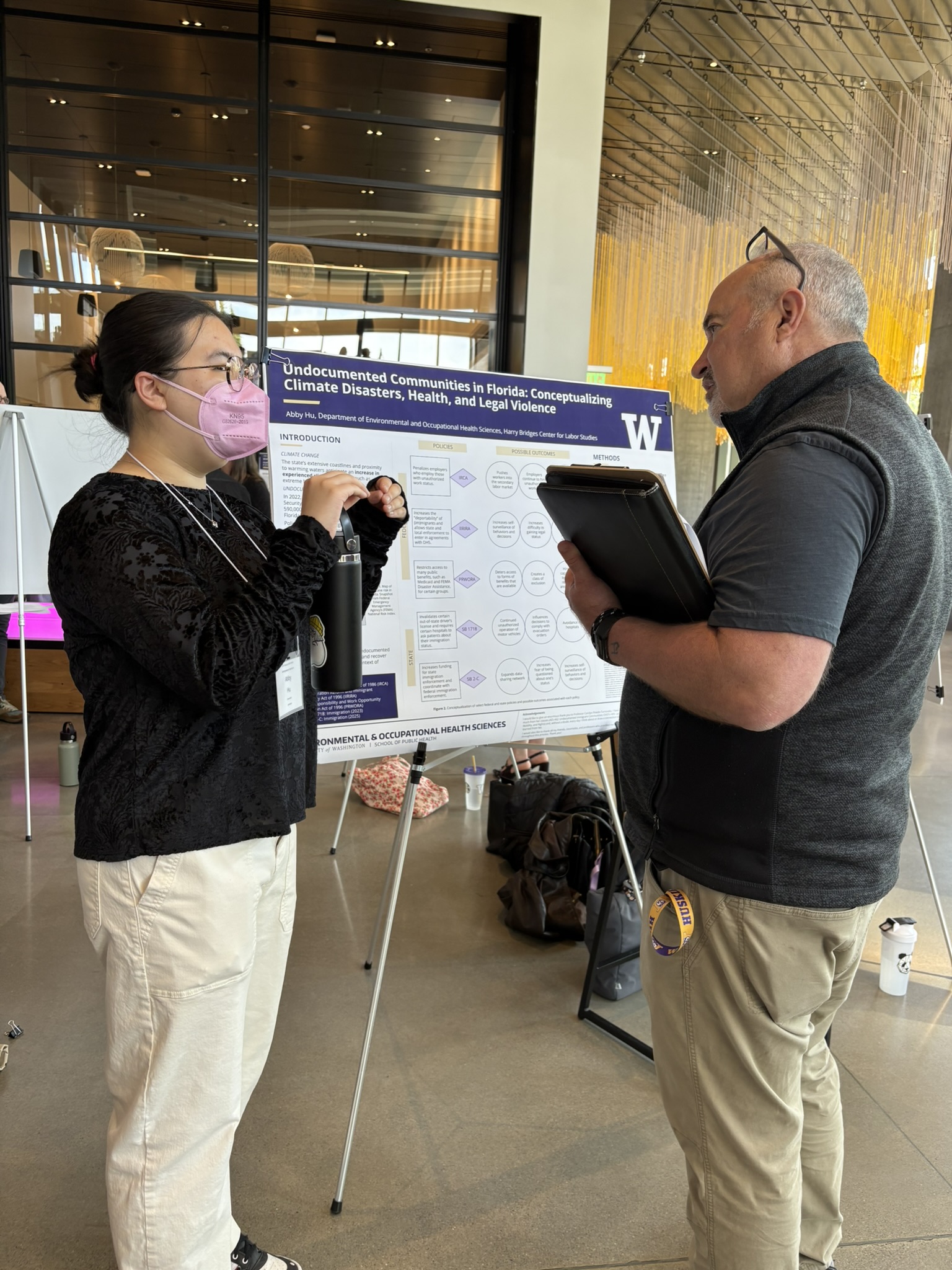 Two people stand facing each other talking in front of a research poster. One is wearing an N95 mask.