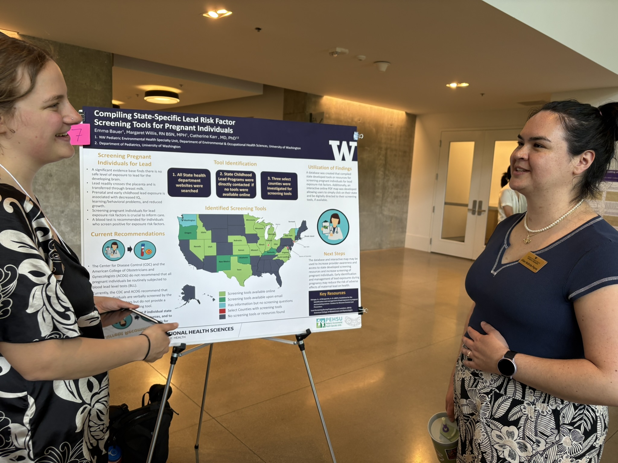 Two people smile standing facing each other in front of a research poster.