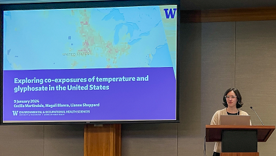 Cecilia Martindale stands at a podium, a screen next to hershows a map and reads, "Exploring co-exposures of temperatures and glyphosate in the United States"