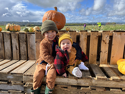 Two young kids pose with a pumpkin.