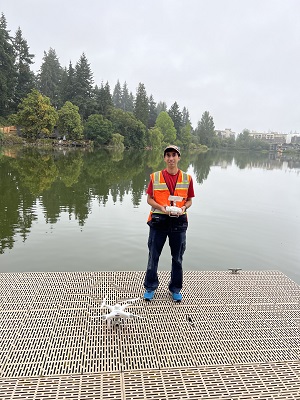 Teresi stands on a dock with drone equipment with lake in the background.