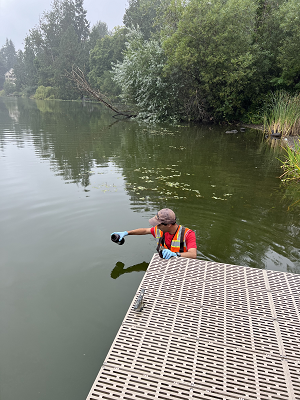 Teresi stands in a lake holding out a sampling bottle over the surface of the water.