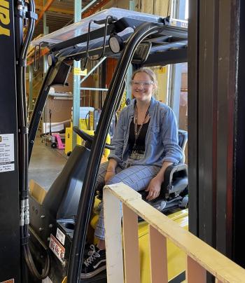 A woman sits on a forklift in a manufacturing plant.
