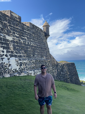 Rivera-Gonzalez stands in front of an old fort with a view of the ocean.