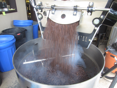 Coffee beans pouring out of a roaster with vapor rising off them