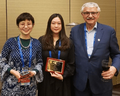 Three people stand together. In the middle, Sarah Kim holds her award.