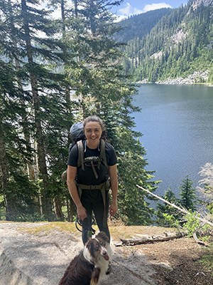 Schollaert stands with a dog in a forest above a lake.