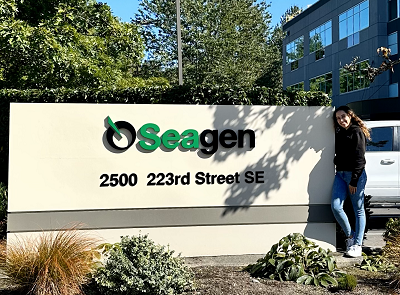 Tania stands outside in front of a sign for the biotech company Seagen.