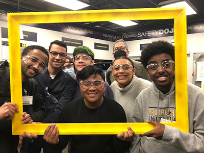 Students from the Brotherhood Initiative and DEOHS Teaching Professor Martin Cohen smile in a group while holding up a picture frame.